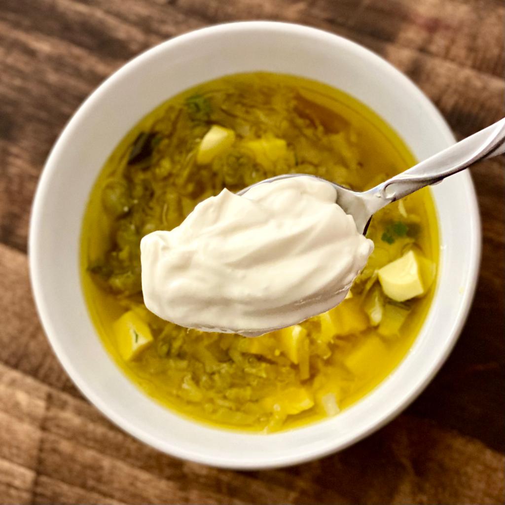 bowl of yellow holodnik with a spoon of sour cream