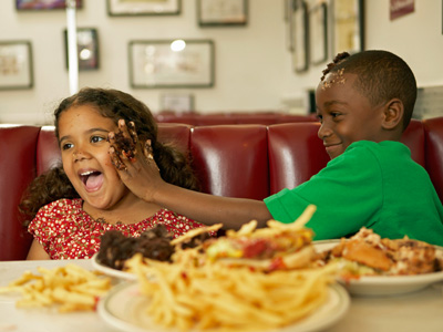 two kids having a food fight over burgers and fries at a diner